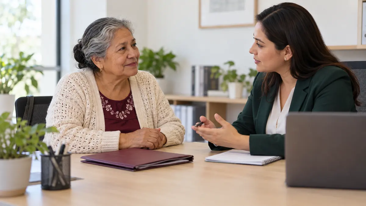 Mujer mayor que conversa con una persona asesora mientras revisan una carpeta familiar.